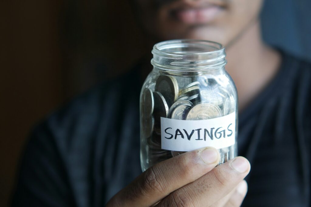 person holding a glass jar labeled savings filled with coins