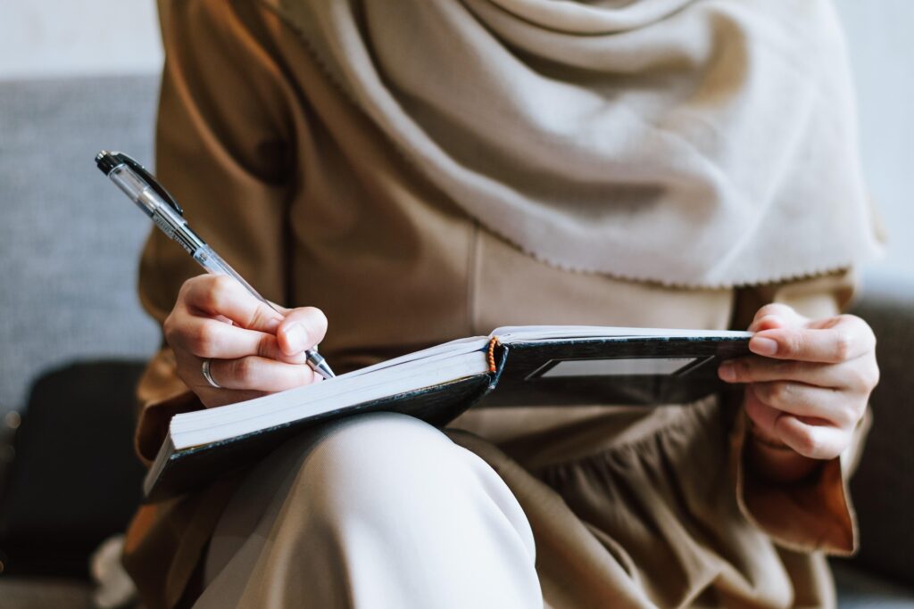 Person writing in a planner notebook while holding it on their lap