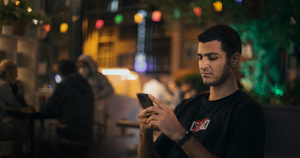 Man checking his phone at night with city lights in the background
