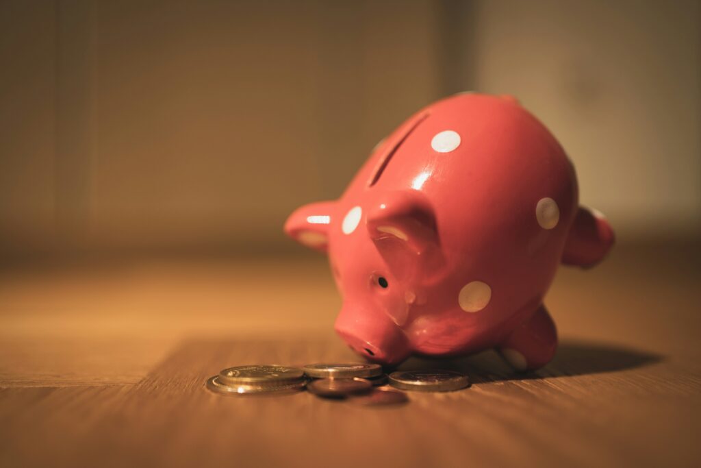 Pink polka-dot piggy bank with a small pile of coins on a wooden surface