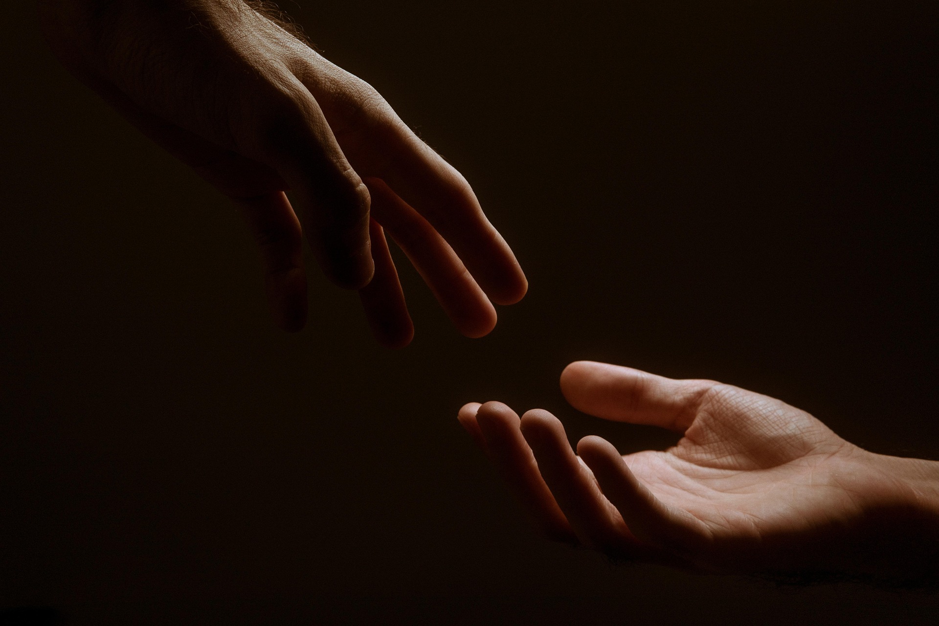Two hands reaching toward each other in dim, warm light