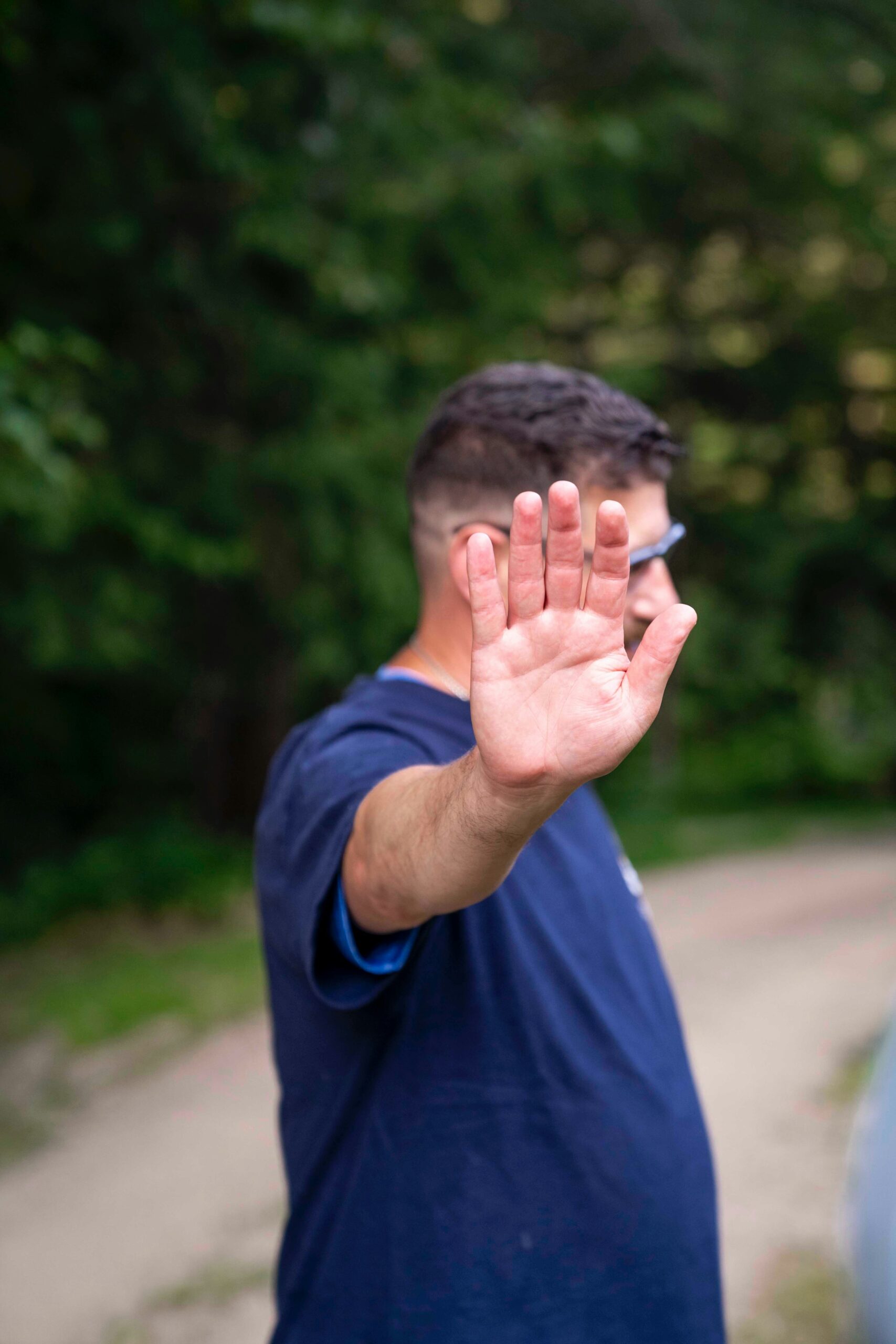 A raised hand in a stop gesture with a blurred figure behind it outdoors