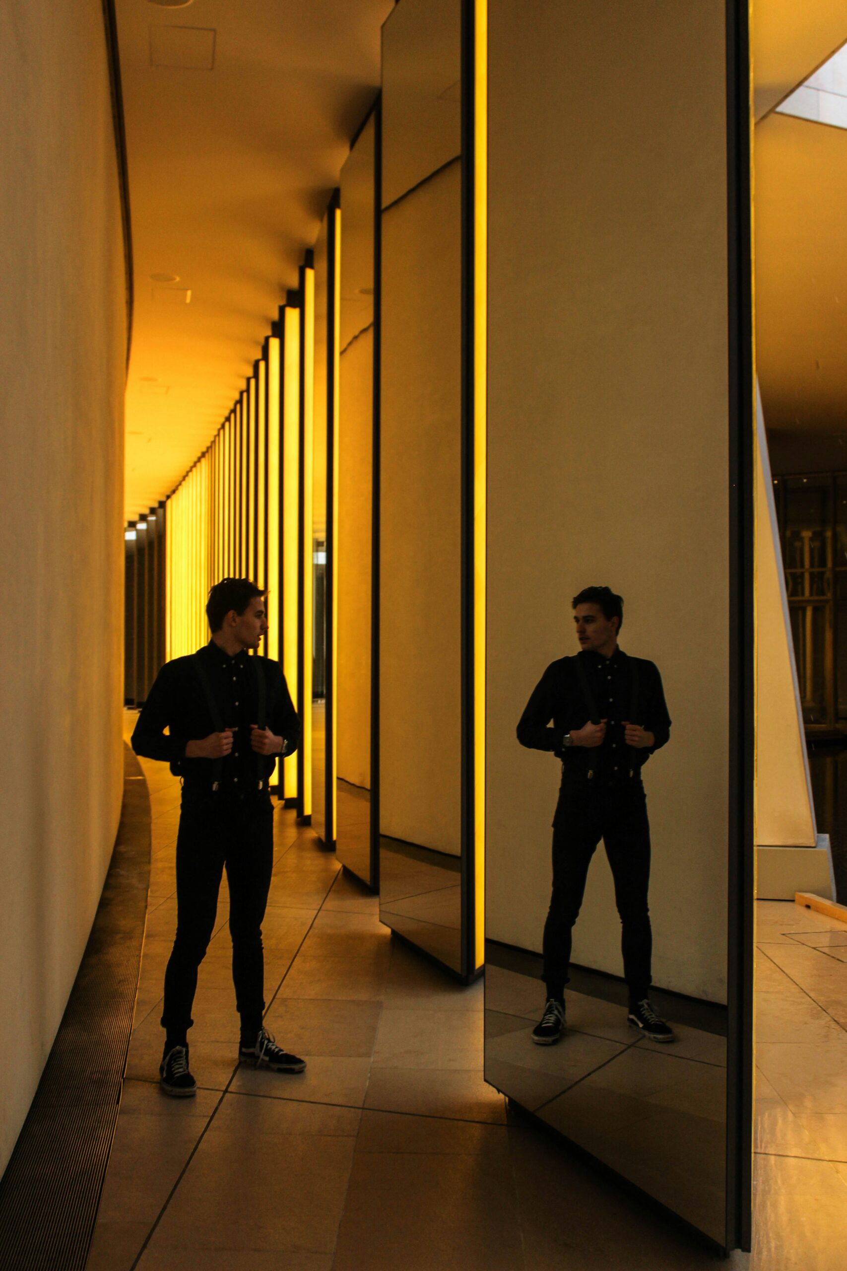 Man reflected in a row of mirrored panels in a softly lit hallway