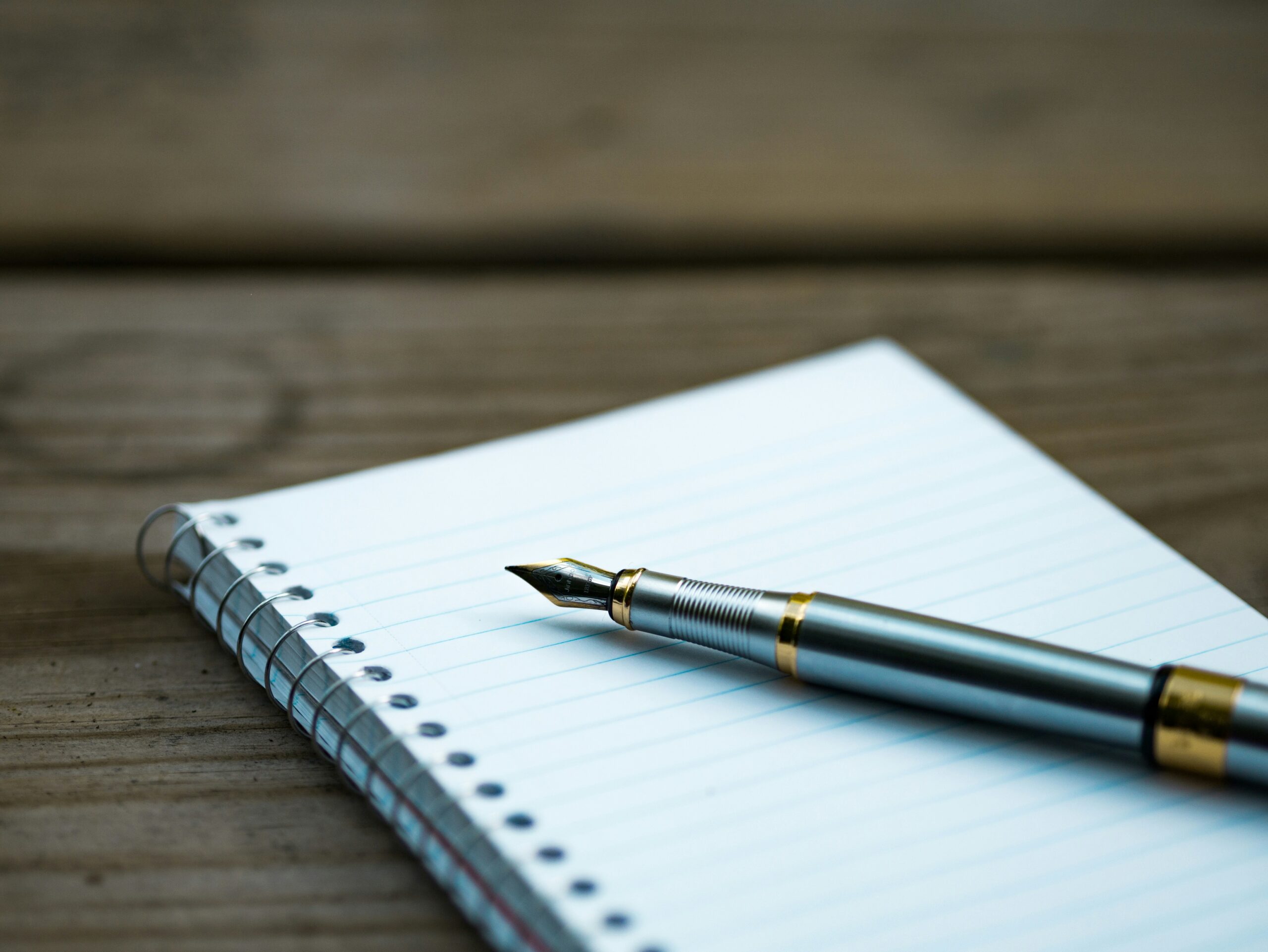 A fountain pen resting on an open notebook on a wooden table