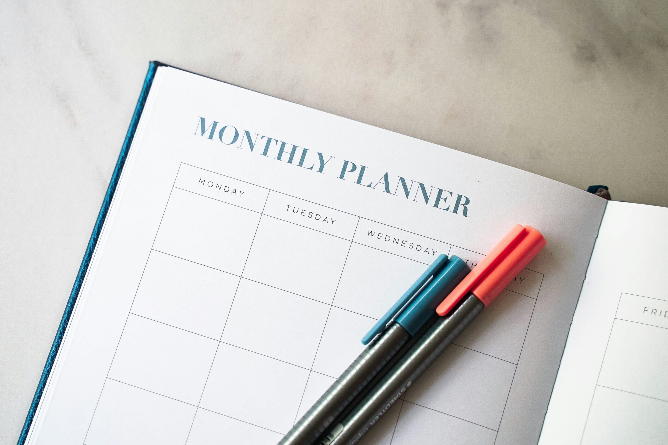 Monthly planner notebook with colorful pens, representing