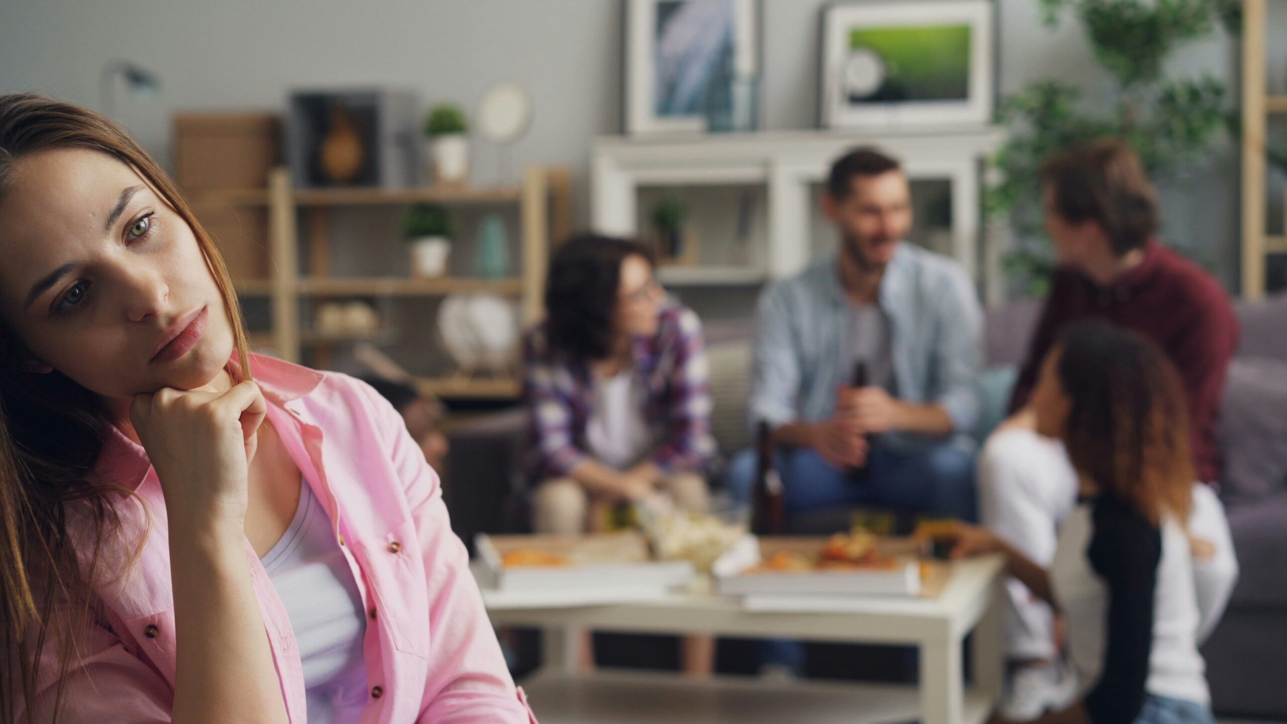 Woman looking thoughtful in the foreground while a family gathering continues blurred in the background