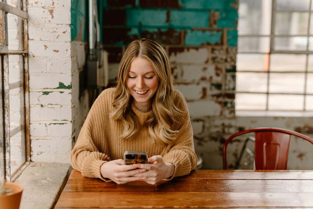 Woman smiling while typing a message on her phone at a café table
