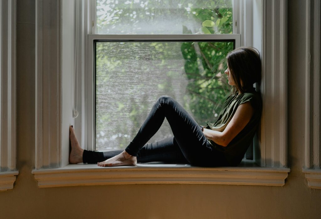 Woman sitting on a windowsill looking out thoughtfully at the trees