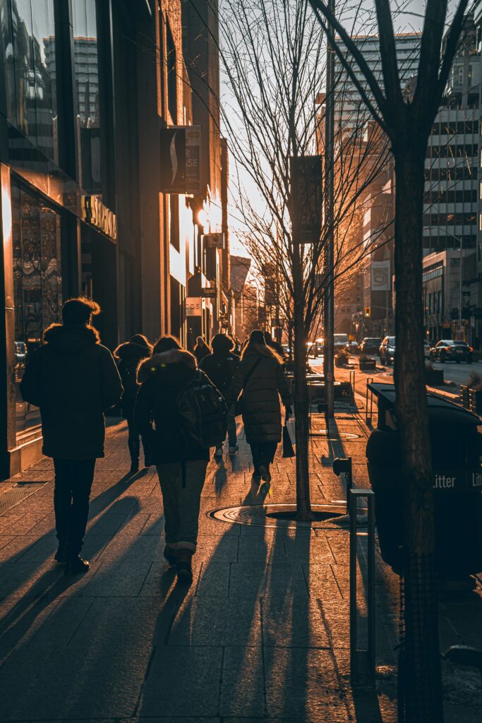 Silhouettes of people walking down a city sidewalk at sunset